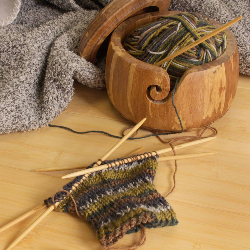knitting needles on floor with yarn in a wooden container