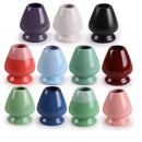 A collection of ceramic matcha tea whisk holders in various colors including black, blue, green, pink, purple, red, white, and brown.